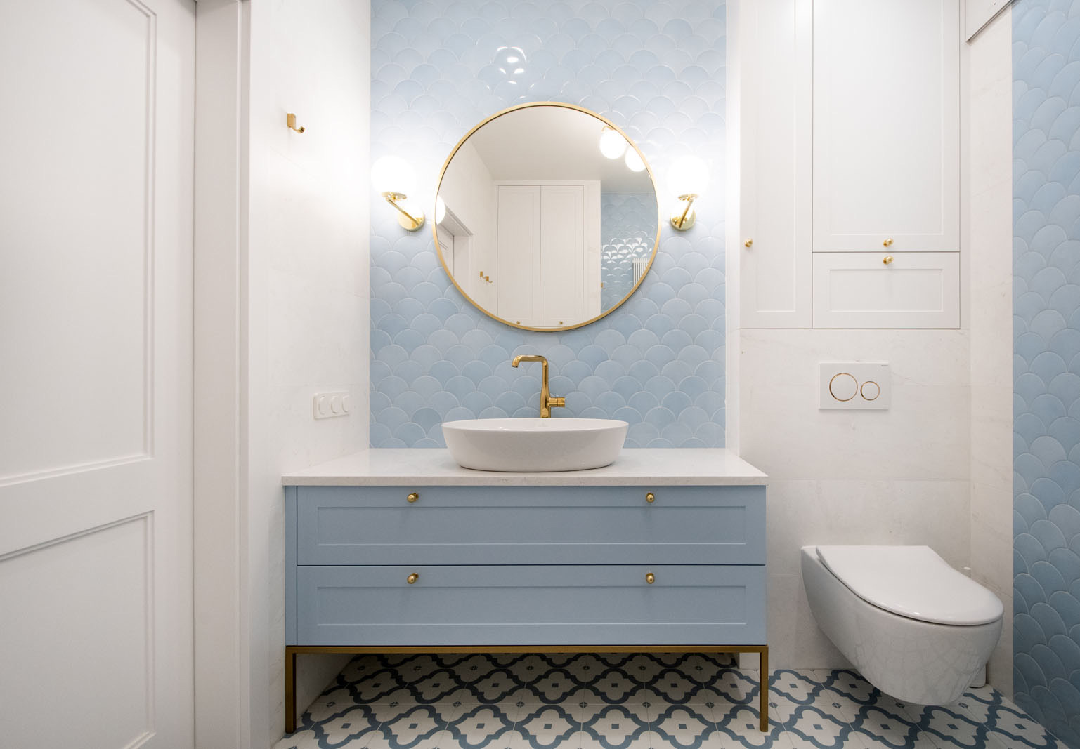 okrągłe lustro w złotej ramie nad umywalka w niebieskiej łazience