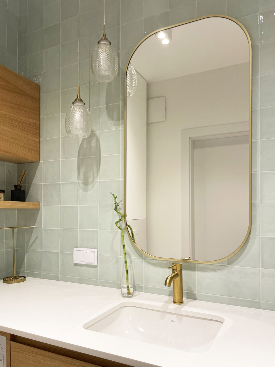 lustro w złotej ramie z zaokrąglonymi narożnikami nad umywalką w zielonej łazience