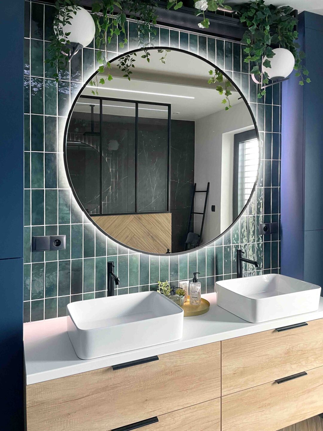 okrągłe lustro w czarnej ramie w łazience nad umywalką z zielonymi płytkami zellige